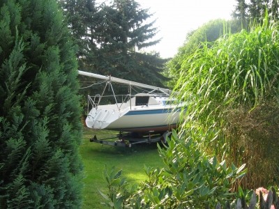 Segelboot mit gelegtem Mast auf einer Wiese in einem Garten. Symbolbild zum Thema Kauf und Eigentum.