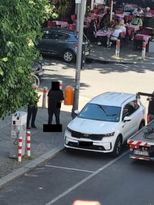 Ein Abschleppwagen steht in Berlin neben einem Pkw. Der Pkw blockiert eine Ladesäule. Der Fahrer spricht mit einer Mitarbeiterin des Ordnungsamtes.